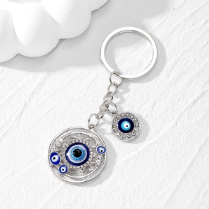 Macro detail of silver Evil Eye keychain with blue gems on a white stone background