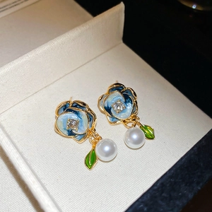 Macro view of blue enamel flower earrings with pearls and green leaf detail
