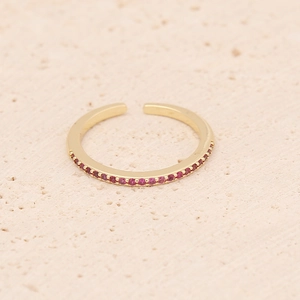 Détail d'une bague dorée ajustable sertie de zircons rouges sur un fond en pierre claire