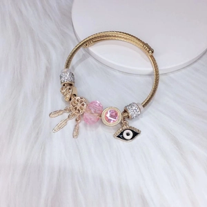 Gold dreamcatcher charm bracelet with pink crystals and evil eye on plush white background