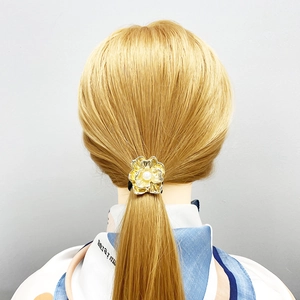 Detailed view of a gold flower hair tie with central pearl worn on a ponytail
