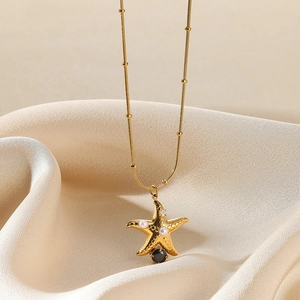 Detail of a gold starfish necklace with pearls and black gemstone on silk fabric