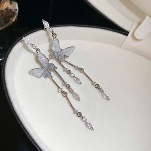 Détail de boucles d'oreilles papillon avec pompons en zircone sur velours blanc luxueux