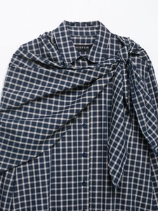 Detail of navy blue plaid shirt featuring a draped scarf-collar design on a flat surface