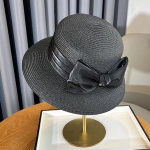 Detail of black straw sun hat with large satin bow on a golden display stand