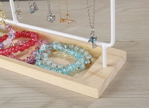 Detail view of white jewelry stand with wooden base holding necklaces and bracelets