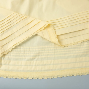 Detail of yellow fabric featuring intricate horizontal pleats and floral lace embroidery trim
