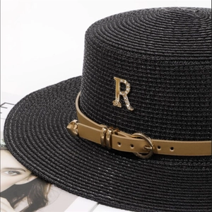 Détail du chapeau de paille noir avec ruban en cuir marron et lettre R sertie de strass