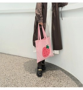 Detailed view of pink canvas tote bag featuring cute red embroidered strawberry patterns