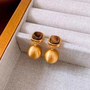 Detail of square gold leopard print earrings displayed in a velvet jewelry box