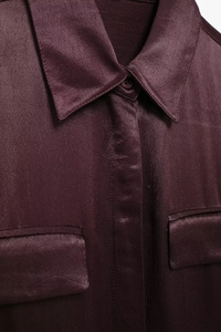 Detail shot of a dark burgundy satin shirt featuring pointed collars and front pockets