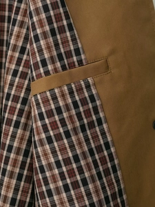 Detail of a brown trench coat featuring classic red and black plaid lining and precise stitching