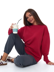 Oversized dark red crewneck sweatshirt with grey sweatpants on a sitting model