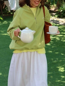 Sudadera verde de mujer con media cremallera y bordado en un entorno de jardín exterior