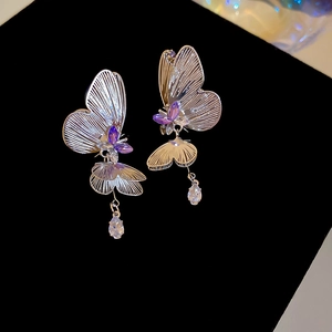 Detailed macro view of butterfly drop earrings with purple rhinestones on black velvet