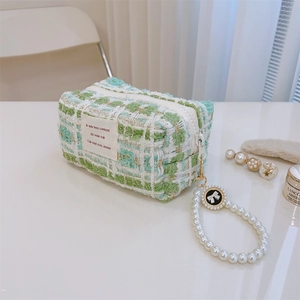 Detail of tweed makeup bag with pearl handle and golden zipper on white surface
