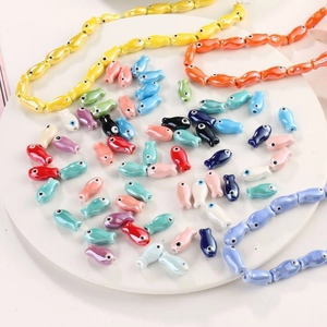 Colorful fish-shaped ceramic beads for DIY jewelry making displayed on a white plate
