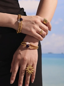 Detail of 18k gold-plated beads bracelet with cross charm and bohemian rings set