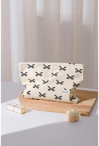 Detail of a cream cotton makeup bag with black bow patterns and a woven logo label