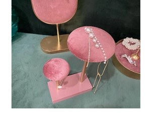 Detail of pink velvet jewelry display stand with golden base and necklace and earrings