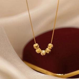 Macro shot of five gold beads necklace with textured finish on elegant silk backdrop