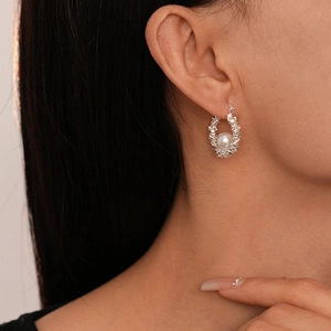 Boucles d'oreilles créoles argentées irrégulières avec une perle blanche sur un modèle