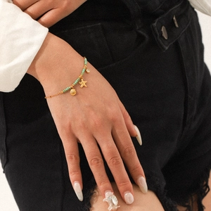 Detailed shot of 18K gold stainless steel starfish and seashell charm bracelet on wrist