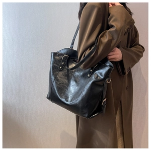 Detail of black tote bag with gold hardware and shiny texture worn by a model