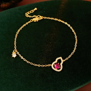 Makroaufnahme eines 18K vergoldeten Hohlkalebassen-Armbands mit rotem Zirkon auf Samtuntergrund