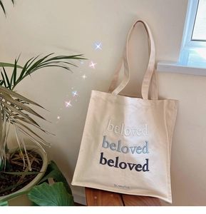 Close-up of three-tone embroidered beloved text on a cream canvas tote bag