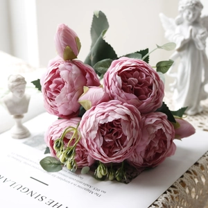 Pink faux peony bouquet with lush petals and green leaves on a lace tablecloth