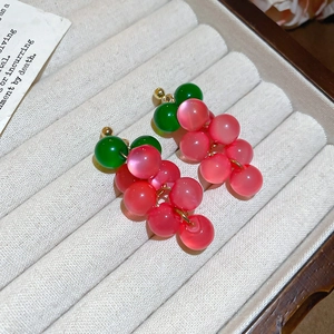 Detailed macro view of resin grape tassel earrings with green leaves on cream velvet tray