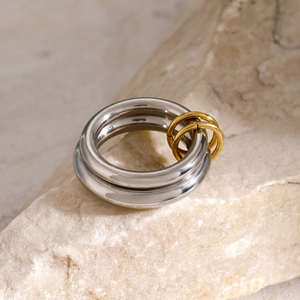 Close-up of polished stainless steel rings with gold accent bands on a natural stone base