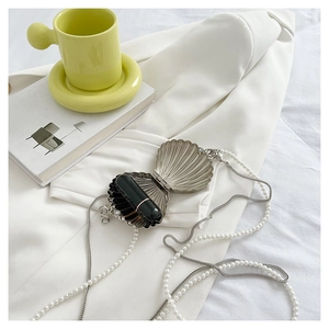 Detail of silver shell bag with pearl chain strap and lipstick storage on white fabric
