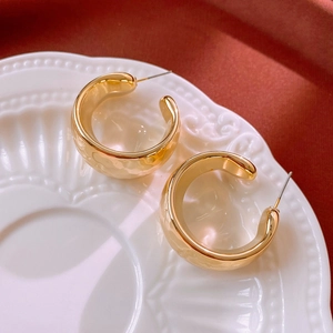 Detail of gold C-shaped hoop earrings with hammer texture on a vintage white plate