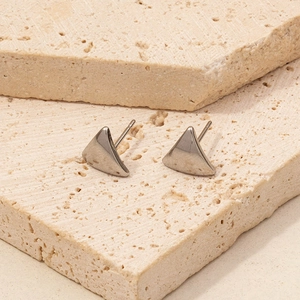 Minimalist silver triangular stud earrings on beige stone display stand with polished finish