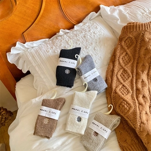 Flat lay of five pairs of warm knitted wool socks with flower embroidery on white bedding