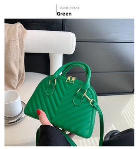 Macro view of green quilted leather shell bag showing V-pattern stitching and gold zipper