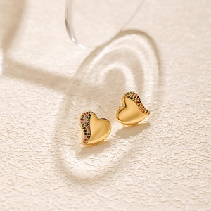 Macro view of gold heart stud earrings with colorful cubic zirconia on sandy background