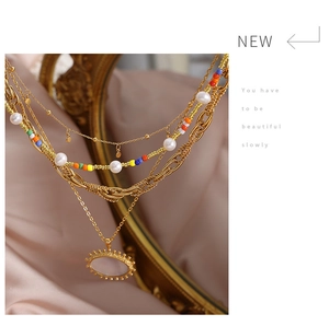 Detail of layered gold titanium steel necklace with colorful beads and sunburst pearl pendant