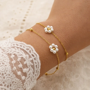 Elegant gold chain bracelet featuring white pearl flowers worn on a lace sleeve wrist