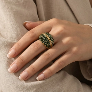Close-up of a wide 18k gold plated ring with emerald green pave-set crystals on a finger