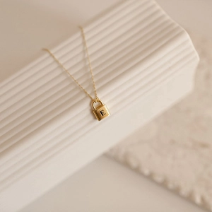 Macro detail of gold lock pendant necklace with engraved letter E on textured stand