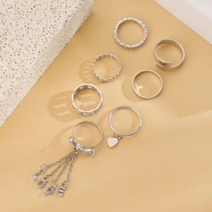 Close-up of silver ring set with love bow pendant and heart charms on beige background
