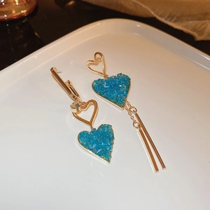 Détail de boucles d'oreilles cœur dorées asymétriques avec cristal bleu sur plateau