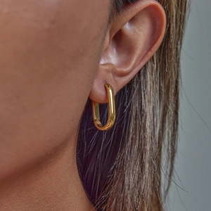 Close-up of a model wearing a minimalist gold-plated rectangular hoop earring