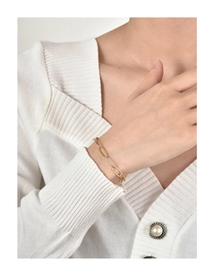 Detail eines vergoldeten Büroklammer-Armbands, getragen über einem weißen Strickärmel
