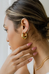 Close-up of golden teardrop hoop earrings worn by a model with a minimalist style