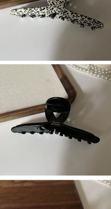 Detail of a large acetate claw clip featuring a black glossy finish and gold text logo