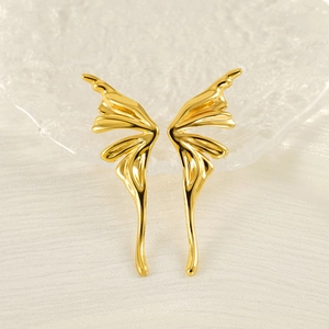 Minimalist gold butterfly wing stud earrings on a textured glass tray and white fabric